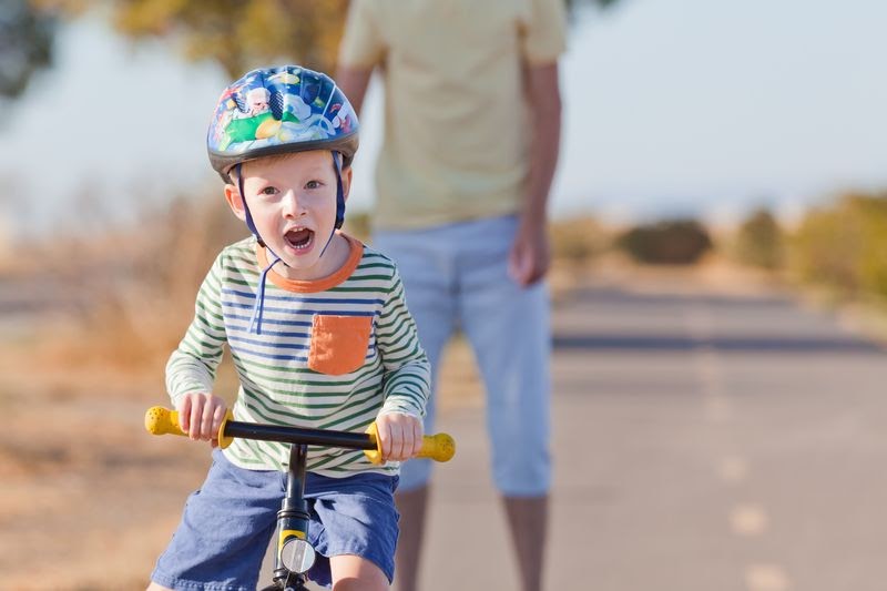 boy wearing a helmet while his dad teaches him how to ride a bike