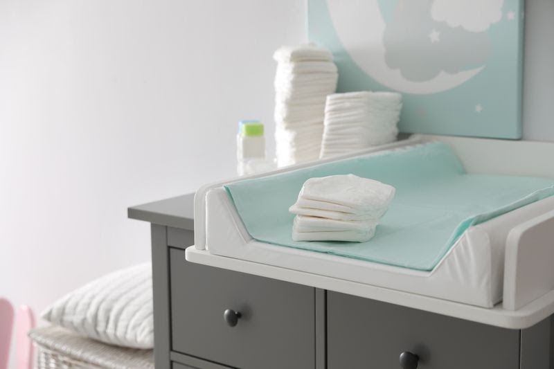 baby changing pad - A white changing pad with a turquoise-colored pad cover sitting on a dark gray drawer