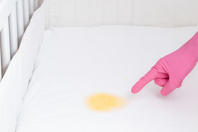 baby crib bedding boy - hand with pink glove pointing to a yellow stain on a white crib mattress