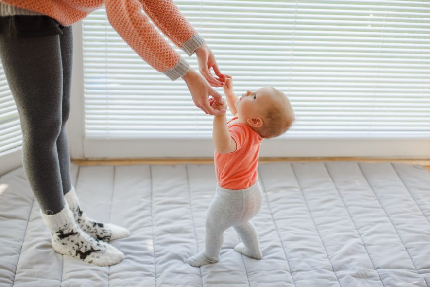 A mom helping her baby walk with baby socks with grips