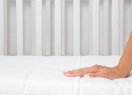 best crib mattress - mother’s hand feeling the texture of a white crib mattress