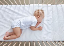 crib bedding sets - An infant sleeping on its side on a white crib bed sheet and mattress