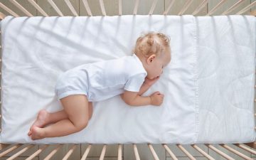 crib bedding sets - An infant sleeping on its side on a white crib bed sheet and mattress