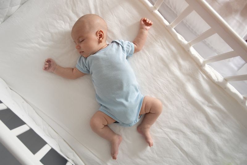 crib bedding sets - An infant in blue clothing sleeping on a comfy crib