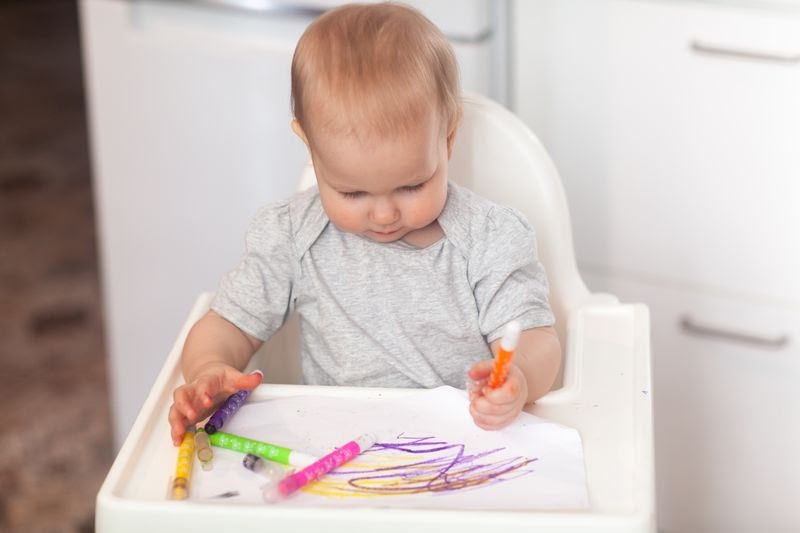 the best high chairs for small spaces - baby using coloring pencils while sitting on a white high chair