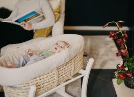 baby lying on a bassinet while a parent is reading a book