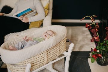 baby lying on a bassinet while a parent is reading a book