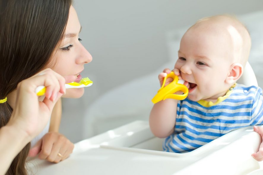 Baby using a teether while the mother shows how to brush teeth