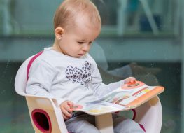 A boy reading a book on a toddler seat