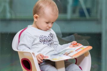 A boy reading a book on a toddler seat