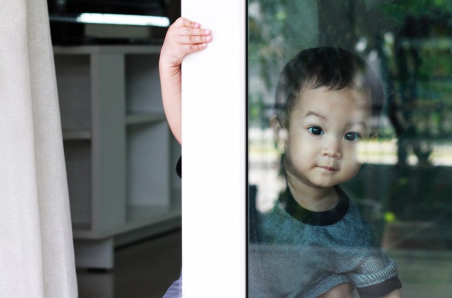 A boy holding onto the sliding glass door while looking out the glass door