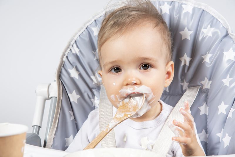 Baby eating puree with a wooden baby spoon