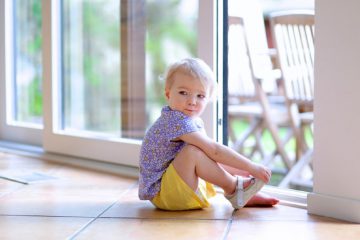A little girl wearing her shoes by the sliding glass door