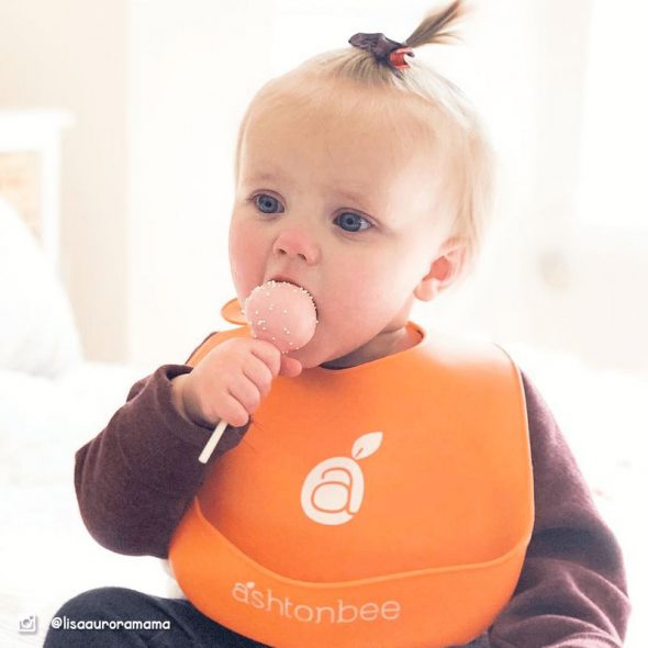 silicone bibs - A baby wearing an orange Ashtonbee bib while eating a lollipop