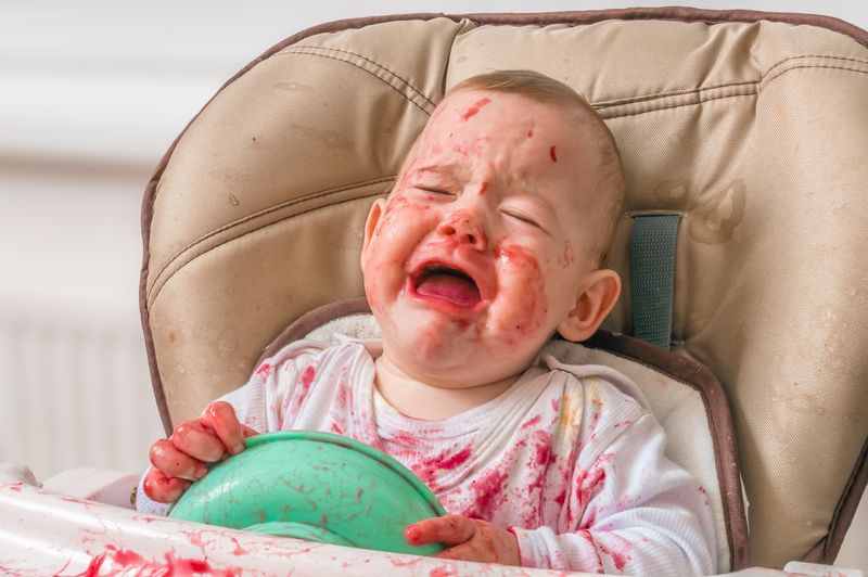 silicone bibs - A crying baby on a high chair with red soup all over its shirt and face