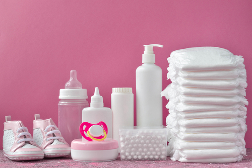 a picture of baby shoes, bottles, diapers, and a pacifier in front of a pink background
