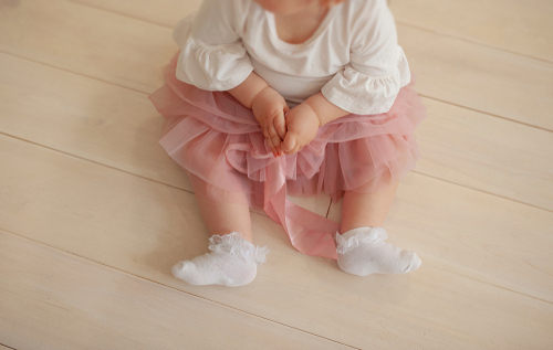 infant sitting on wooden floor with baby girl socks and tutu on