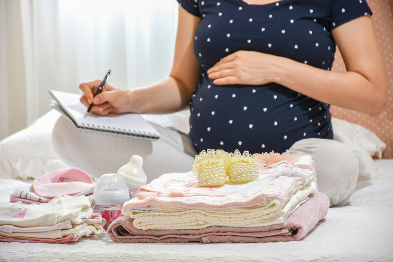 things to buy for second baby - half body view of pregnant woman making a checklist in front of baby supplies