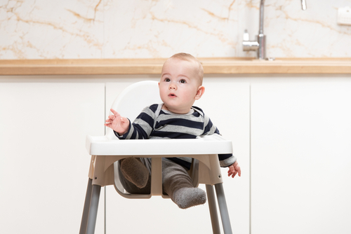 Happy Baby Sitting in High Chair in a White Kitchen
