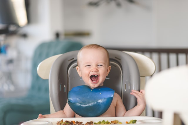 a smiling baby sitting on a high chair with food on the tray
