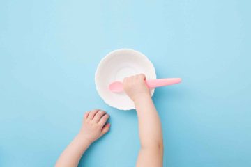 baby feeding spoon - top view of baby’s hand holding a pink spoon on a bowl