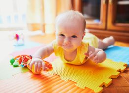 Baby lying on top of foam playmats with toys in hand.