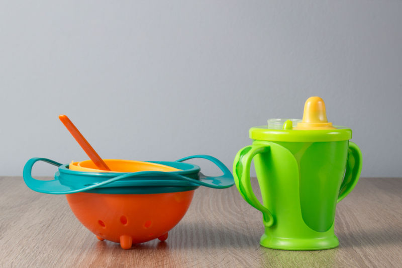 Baby bowls and spoons, and sippy cup next to each other.