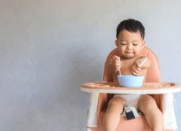 Baby eating on his own on a high chair.