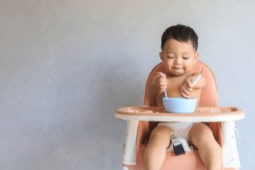 Baby eating on his own on a high chair.