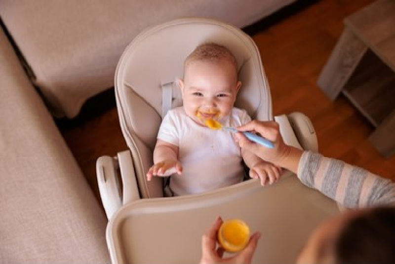 A mother feeds a baby in a high chair with baby food.