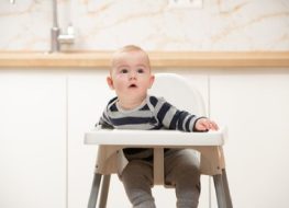 When to stop using high chair - Baby looking up from a plastic high chair.