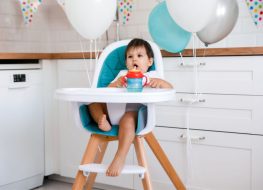 A toddler drinking from his straw sippy cup in a wooden high chair
