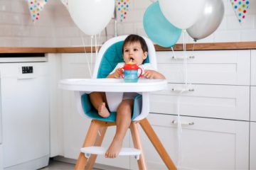 A toddler drinking from his straw sippy cup in a wooden high chair