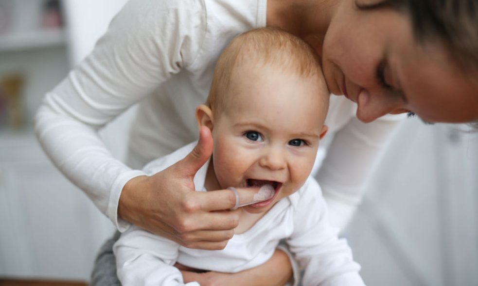 A mother using a finger brush on her baby’s tongue.