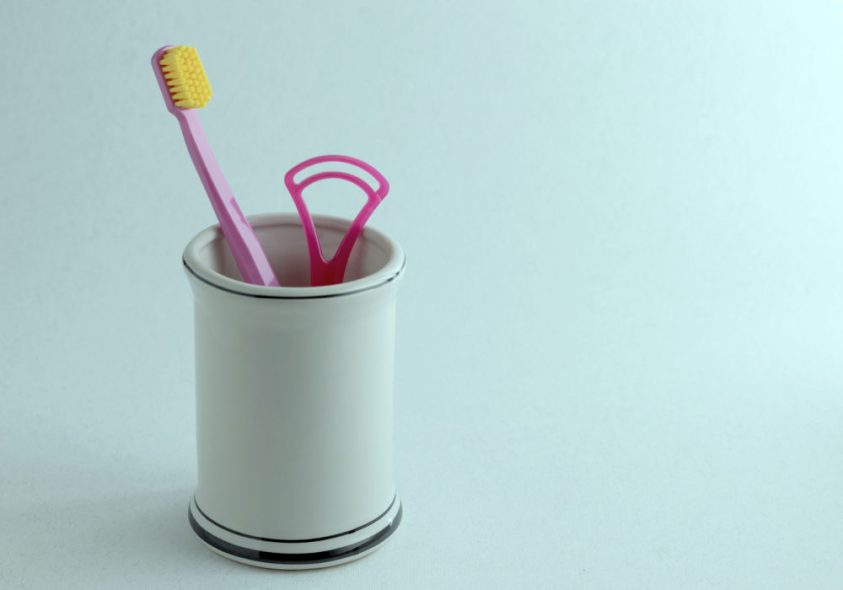 A soft-bristled toothbrush and tongue cleaner next to each other.