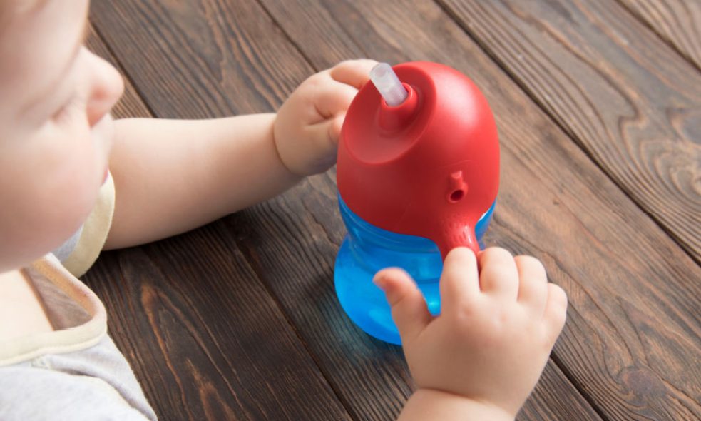 A baby holding a straw sippy cup.