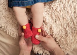 baby legs wearing red sock booties held by two hands