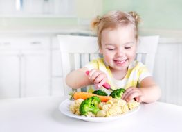 a baby girl digging into a plate full of vegetables