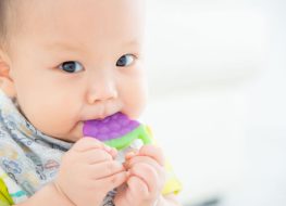 closeup of baby chewing on grape shaped fruit teether.