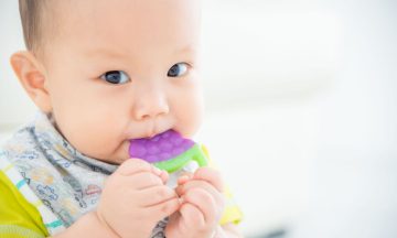 closeup of baby chewing on grape shaped fruit teether.