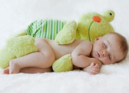 a baby sleeping on his side with a stuffed frog toy cuddling him