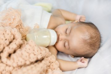 a baby sleeping under a blanket sucking on a bottle full of milk
